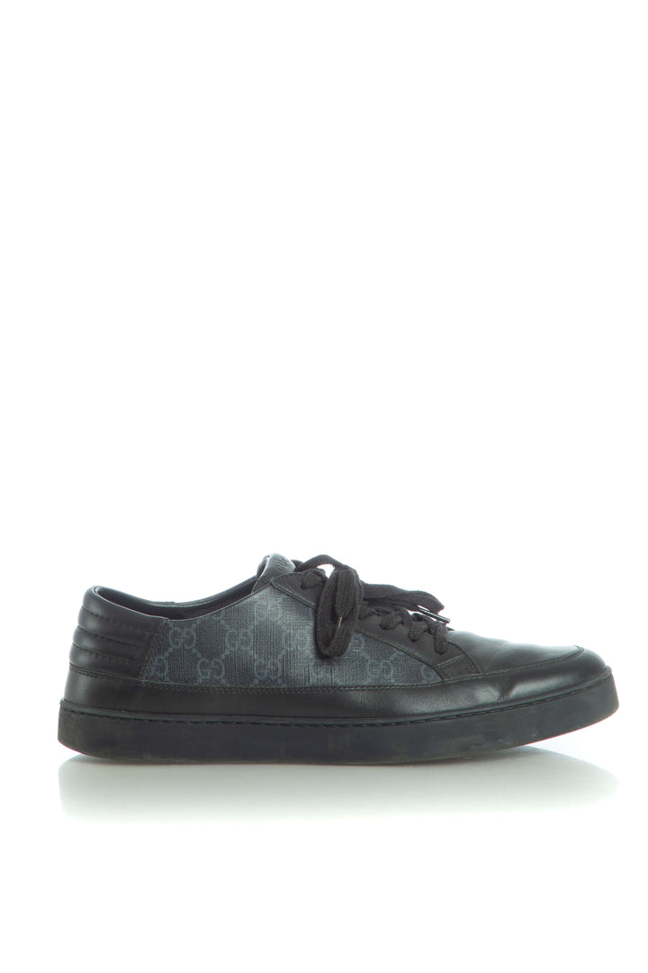 Vista lateral de tenis bajo Gucci en piel negra con paneles GG Supreme
