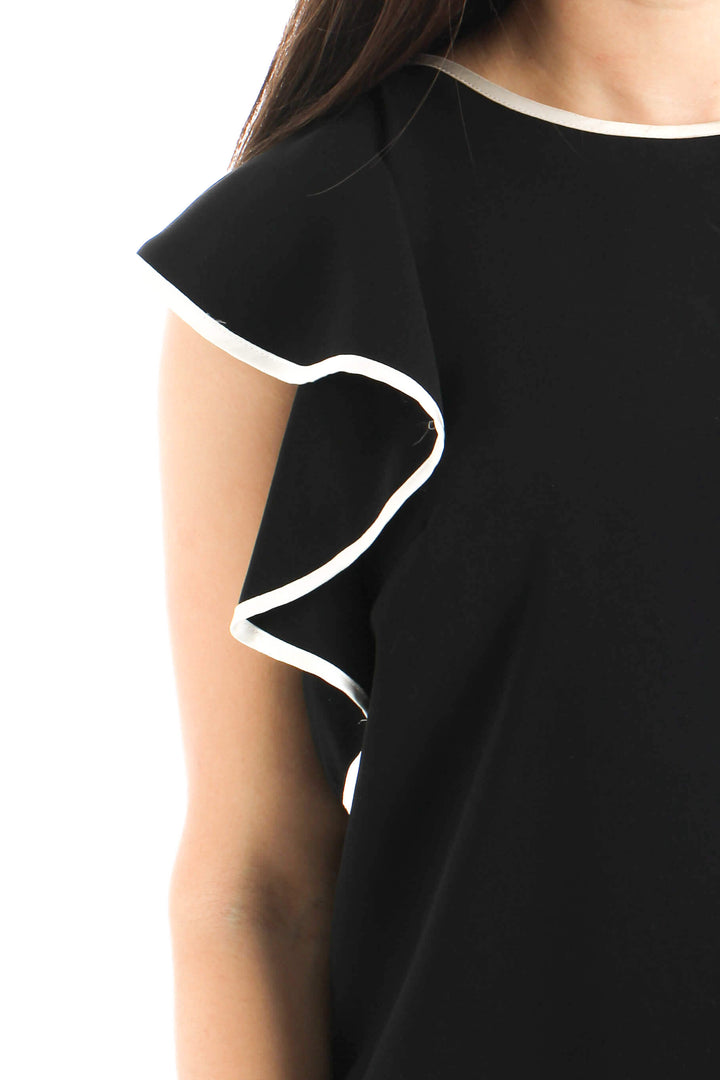 Blusa Amanda Uprichard de seda negra con olanes ribeteados en blanco, detalle del frente